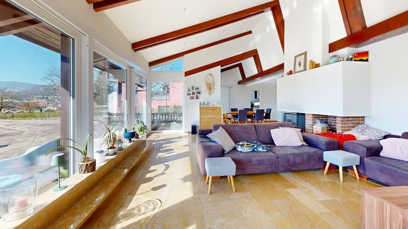 large windows, fireplace, wooden ceiling, wooden floor, two couches, stools, plants, dining table, chairs