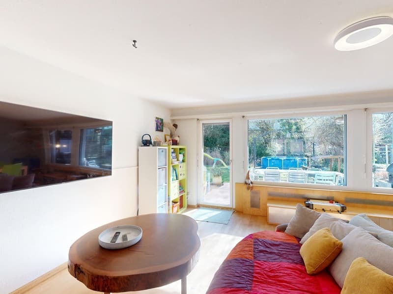 modern living room with large windows, wooden table, couch, TV, bookshelf, and a view of the garden