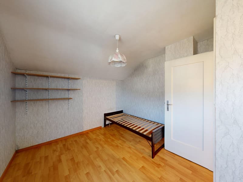 Empty room with wooden floor, white walls, three shelves, a single bed, and a lamp