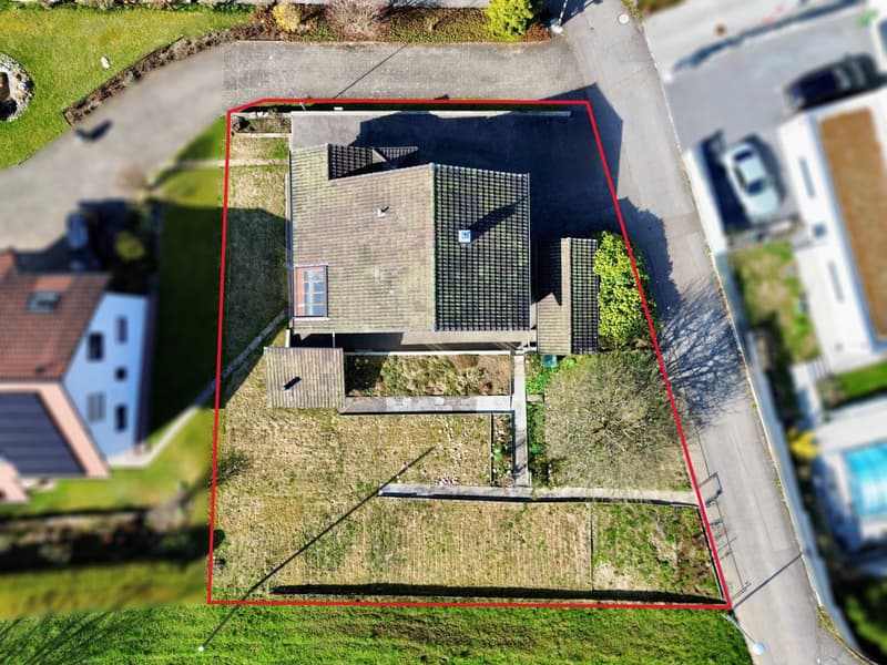 House with a sloping roof, surrounded by a yard, two cars parked on the street, a neighboring house with solar panels