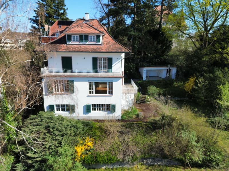 2 story house, white exterior, brown roof, balcony, surrounded by trees and bushes