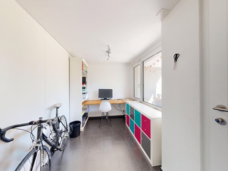 A room with a desk, chair, monitor, storage boxes, and a bicycle