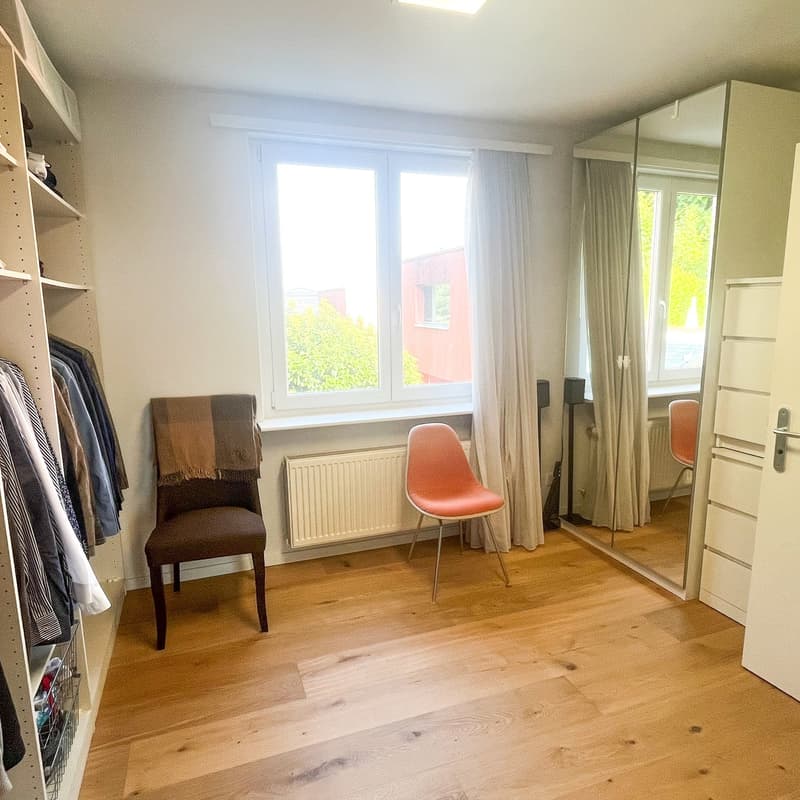 room with wooden floor, white walls, large window with curtains, built-in wardrobe, closet, chair, radiator, mirror, closet