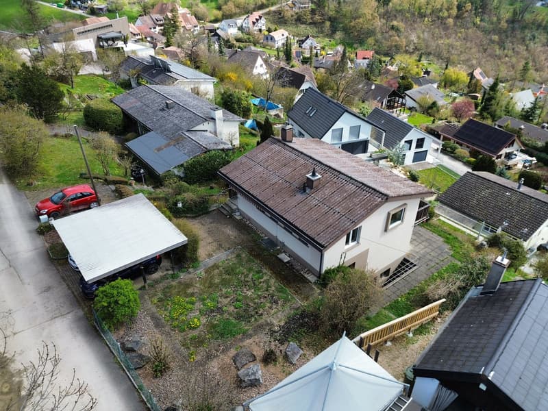 Aerial view of a neighborhood with several houses, one with a red car parked in front, and a carport with a car underneath it.