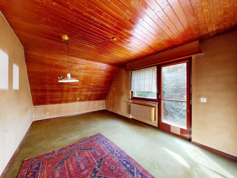 Empty room with wooden ceiling, beige carpet, and a large rug. There is a glass door with a white curtain and a radiator on the wall.