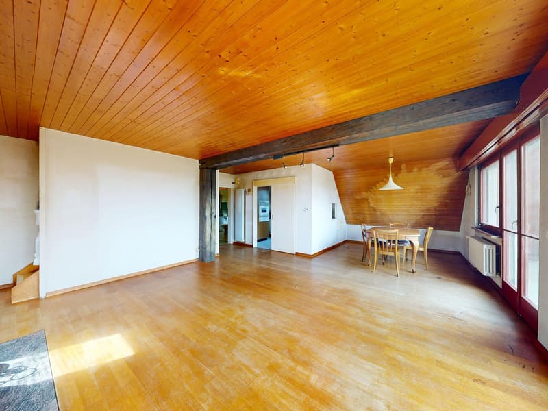 Empty room with wooden floors, wooden ceiling, and white walls. There is a dining table and chairs in the corner.
