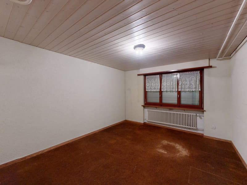 Empty room with white walls, wooden ceiling, brown carpet, a window with white curtains, and a white radiator.