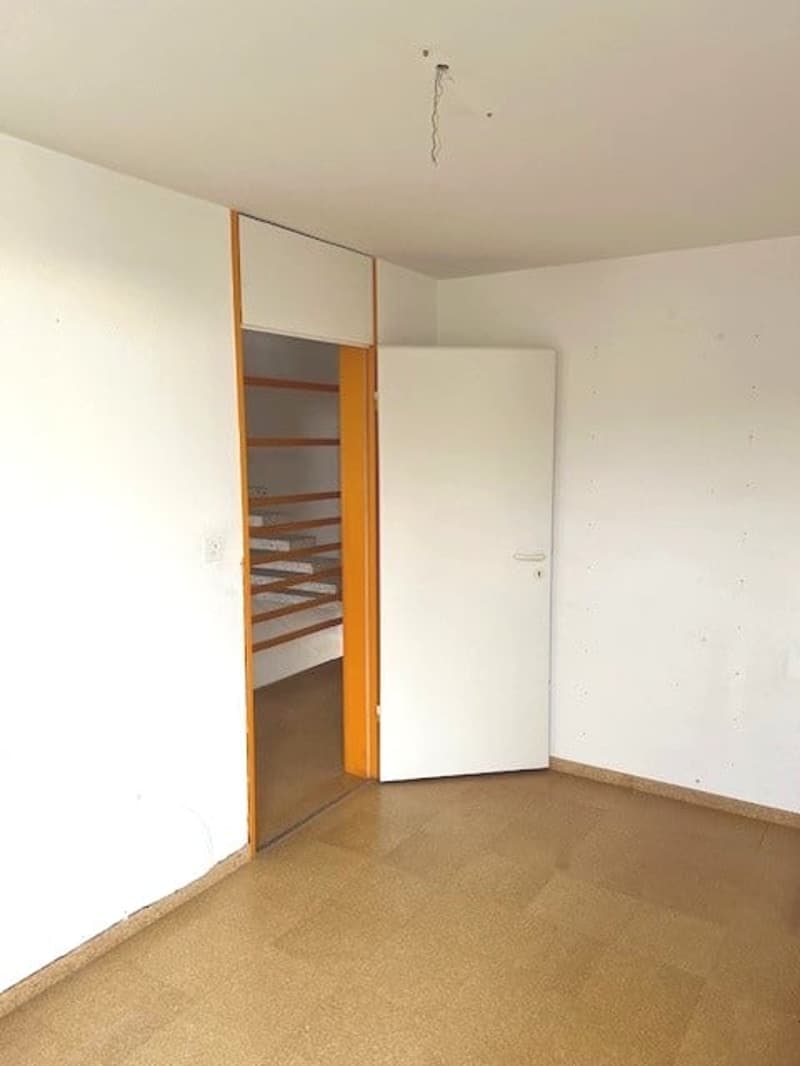 empty room with brown floor, white walls, an orange shelf and an open door