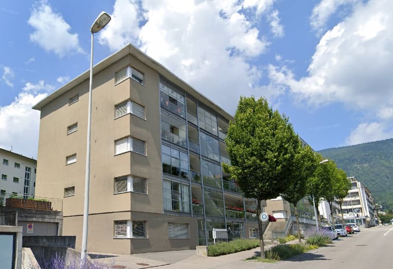 4 story building, glass windows, beige exterior, street light, trees, cars parked