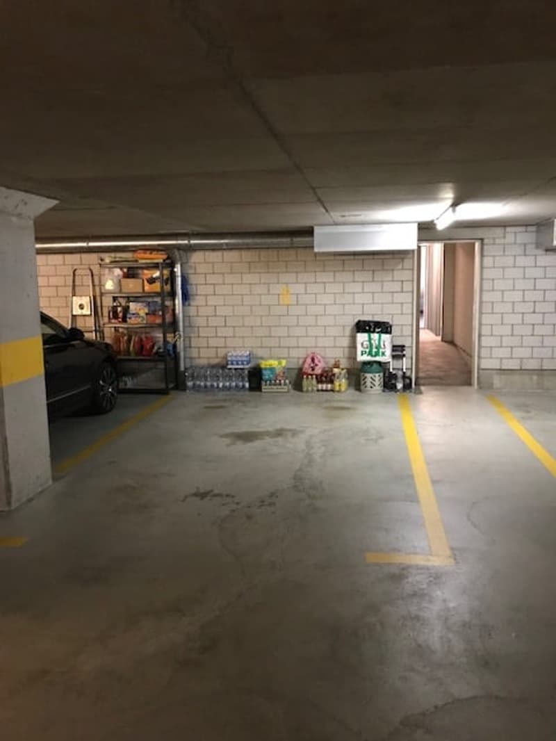 Empty parking space with yellow lines, a car parked, shelves with items, and a door leading to an exit.