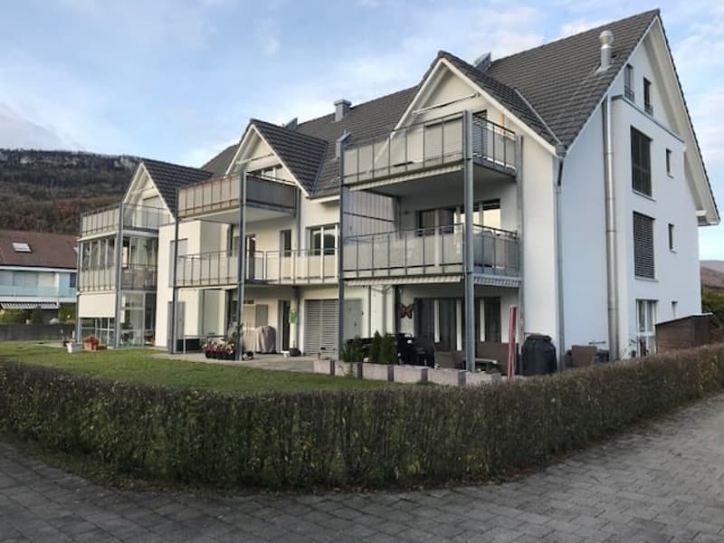 3 story apartment building, white exterior, gray roof, multiple balconies, garden, paved walkway