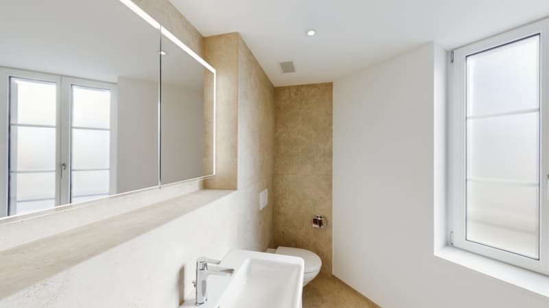 Spacious bathroom with large mirror, white sink, and beige tiled walls. Large window providing natural light.