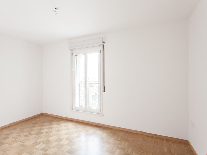empty room, white walls, wooden floors, single window with balcony access