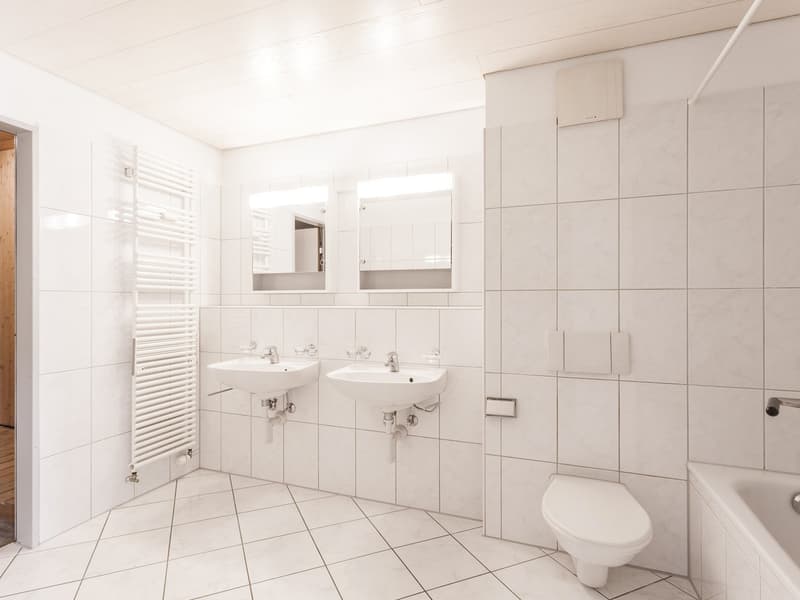 Two sinks, white toilet, white bathtub, white tiles, white mirrors, white towel rack