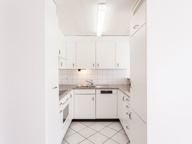 Modern kitchen with white cabinets, granite countertops, built-in oven and dishwasher, gas stove, sink with faucet, under-cabinet lighting, and an integrated fridge.