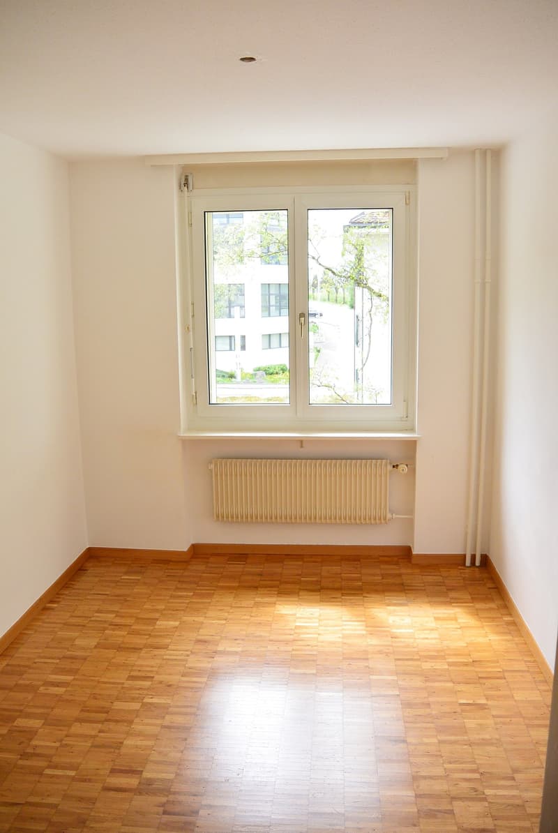 room with white walls and wooden floor, large window, white radiator