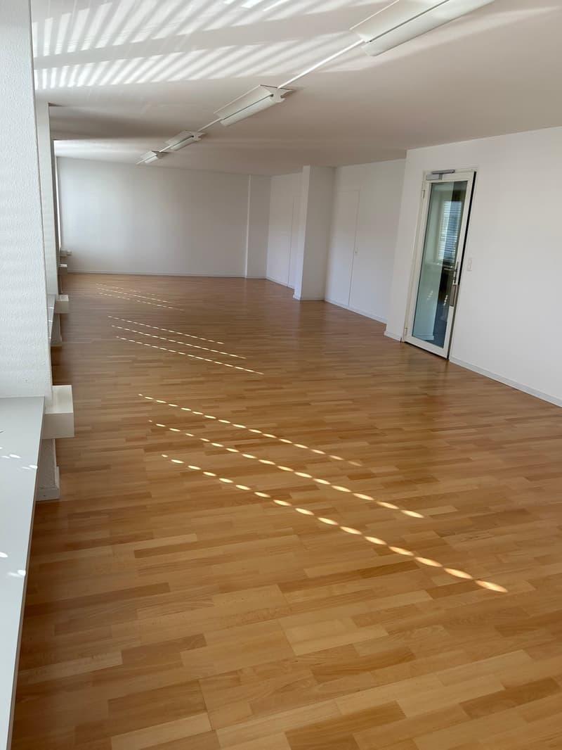 wide, clean, bright space with wooden floor, white walls, overhead lighting, a door