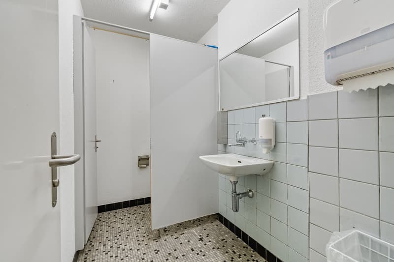 A bathroom with tiled floor, white walls, an open door, a sink with faucet, and a mirror.