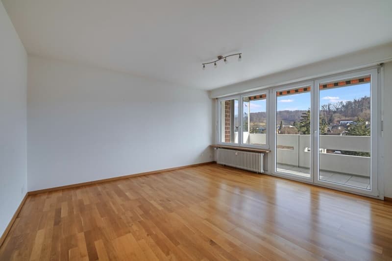 Wohnzimmer mit schönem Parkett, grosser Fensterfront und Zugang zum Balkon