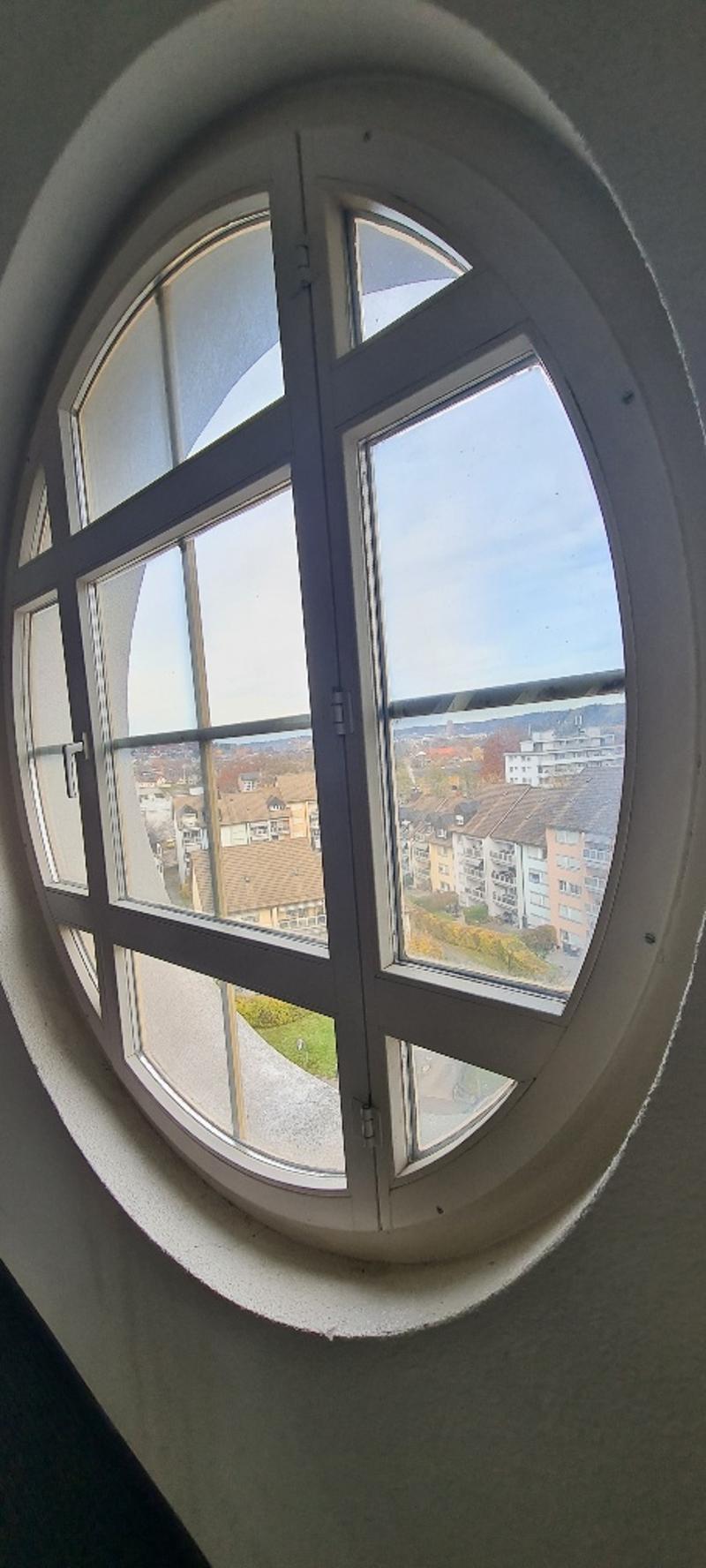 Large round window, providing a panoramic view of the cityscape with buildings and trees