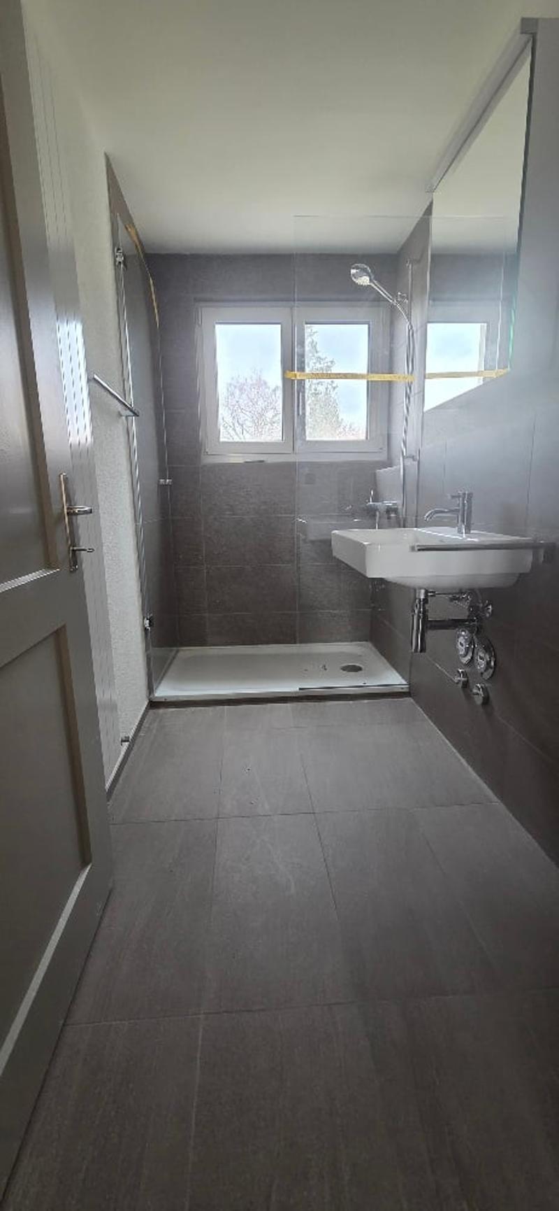 A tiled shower stall, a white sink, a faucet, a mirror, and a window.