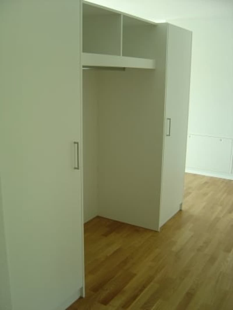 A corner wardrobe with open doors, wooden floor, white walls