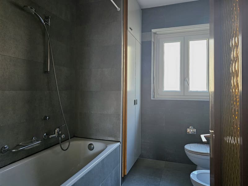 Gray tiled walls, bathtub, white toilet, gray tiled floor