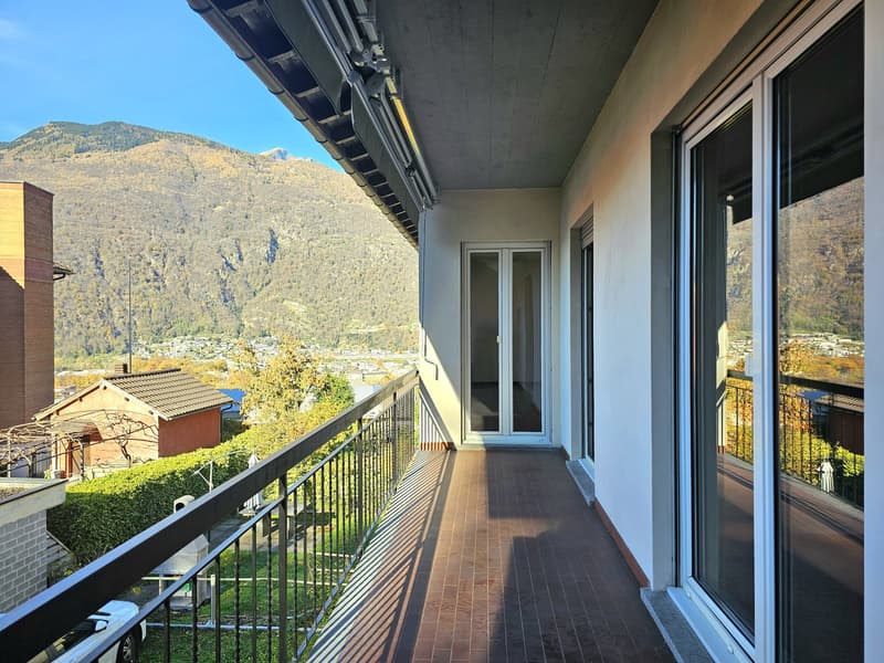 A balcony with a brick floor, a metal railing, and a mountain view in the background.
