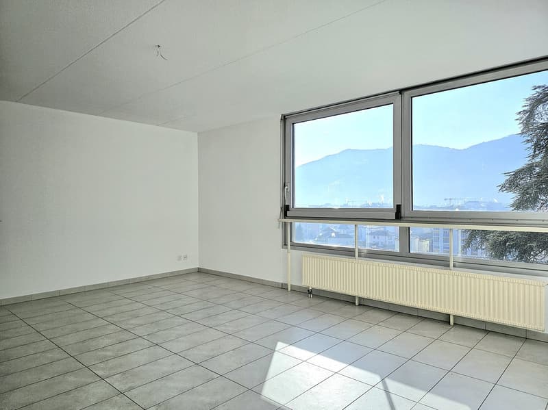 Empty room, white walls, tile floor, large window, balcony railing, mountain view
