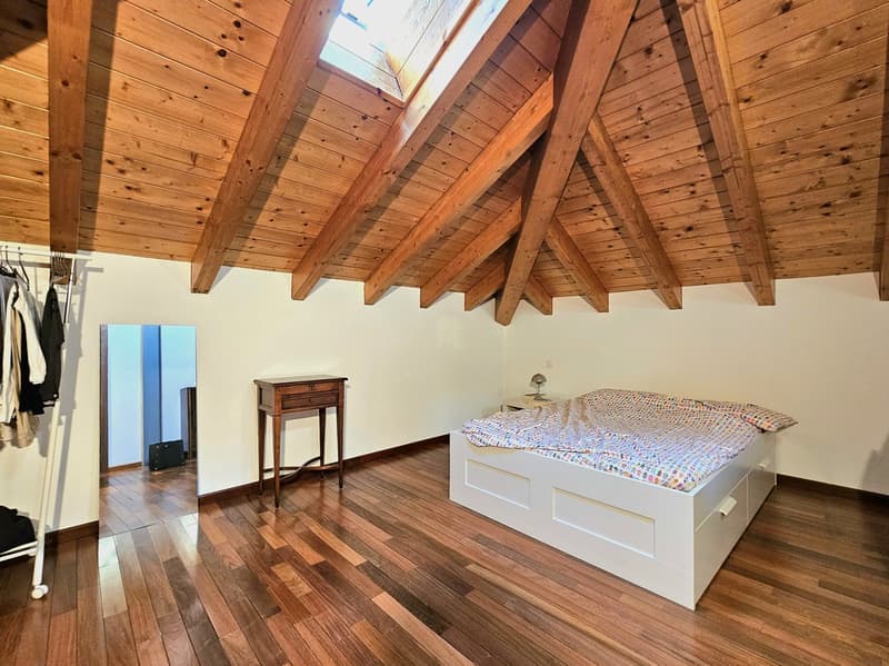 Room with wooden floor, wooden ceiling with beams, skylight, bed, table, side table, wardrobe, mirror