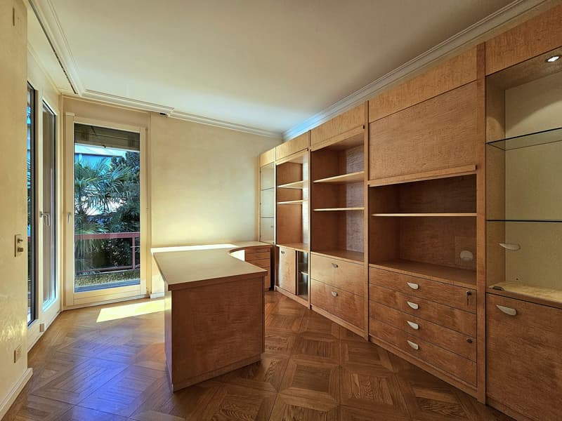 large desk, wooden shelves, large window, balcony with railing