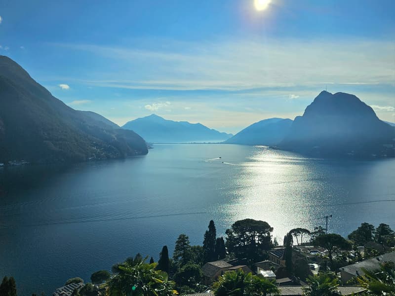Overlooking a serene lake with mountains and clear blue skies, with boats and distant houses