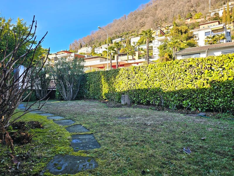 Grass lawn, stone pathway, hedge, building and hill in the background