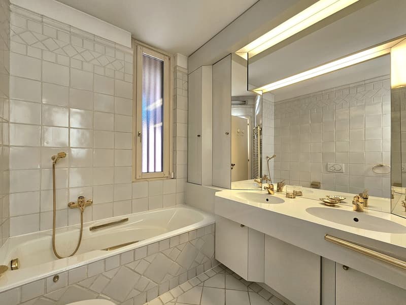 Bathroom with white tiles, bathtub, double sink, mirror, and shower head. Separate WC visible.