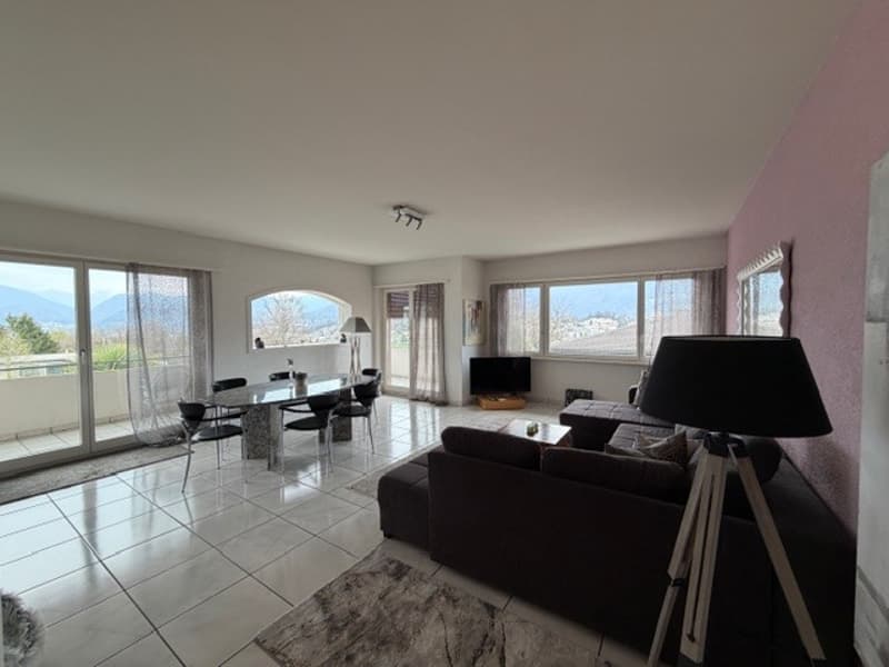 Spacious living room with white tiles, large windows, dining table, chairs, couch, lamp, television, and rug.