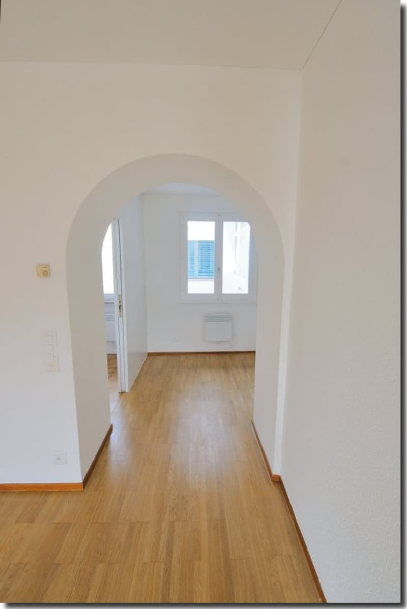 white walls, wooden floor, arched hallway, window