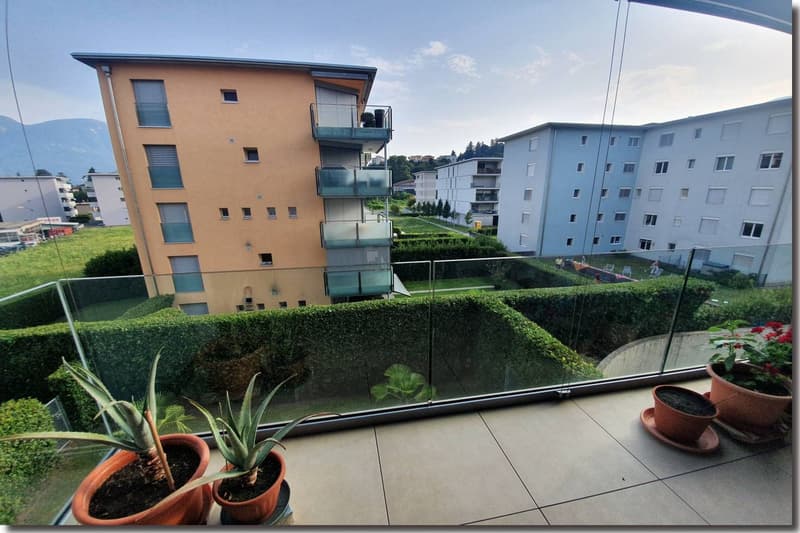 A multi-story building with balconies, glass railings, well-trimmed hedges, and other greenery.