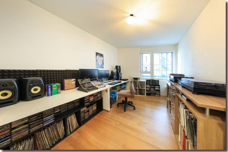 A room with a wooden floor, two speakers on the desk, monitors, keyboard, and chair.