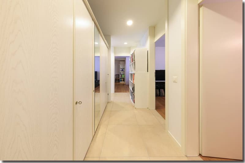 Long hallway with light wooden floor, wooden doors, and white walls