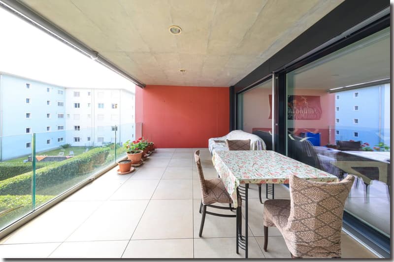 Balcony with tile flooring, glass railings, and outdoor dining setup with chairs and table