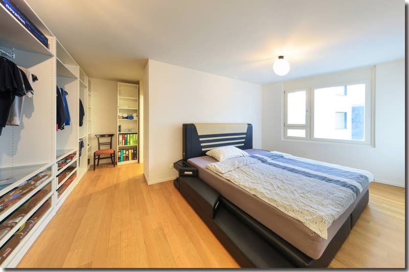 spacious bedroom with wooden flooring, built-in wardrobes, bed with mattress and pillows, nightstand, and large windows