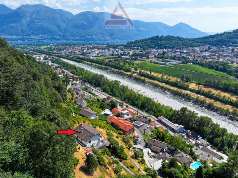 Aerial view of a town nestled in a valley surrounded by mountains, with a river running through the center. The town appears to have a mix of residential and commercial buildings, with some agricultural land visible in the foreground.