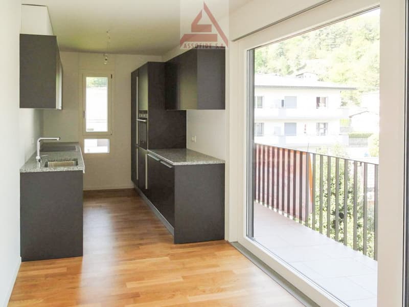 Modern kitchen with dark cabinets, granite countertops, and large windows overlooking a balcony or terrace.