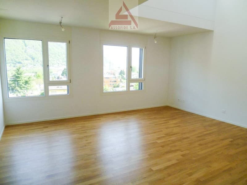 Spacious room with large windows, hardwood flooring, and white walls.
