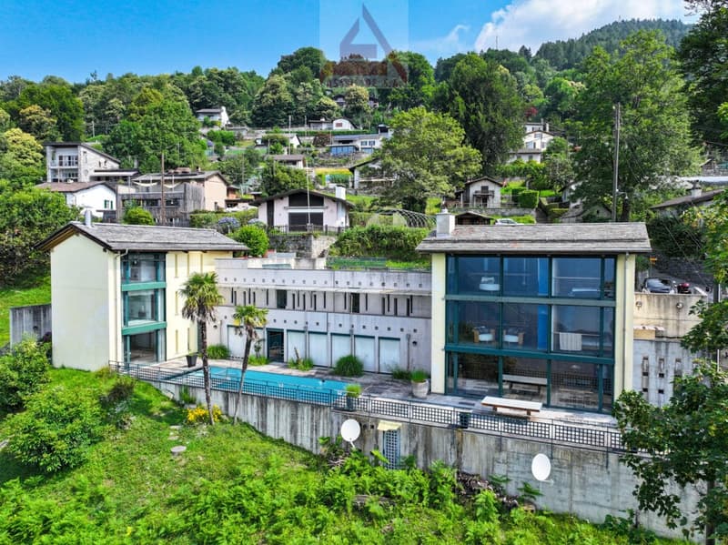 Multi-story building with glass facades, surrounded by lush greenery and trees, located in a hilly, mountainous area