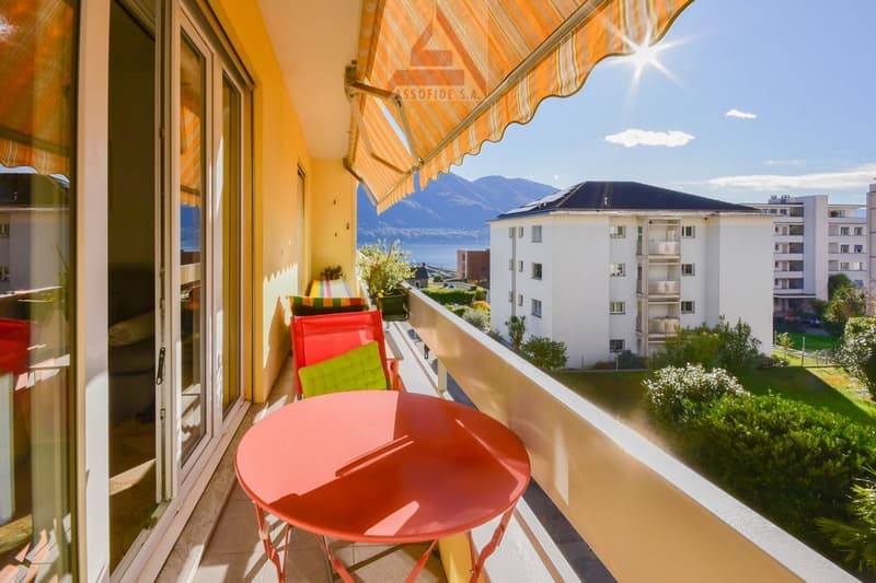 Red table and chairs, yellow wall, orange awning, large glass door, green plants, balcony view of a building and mountains
