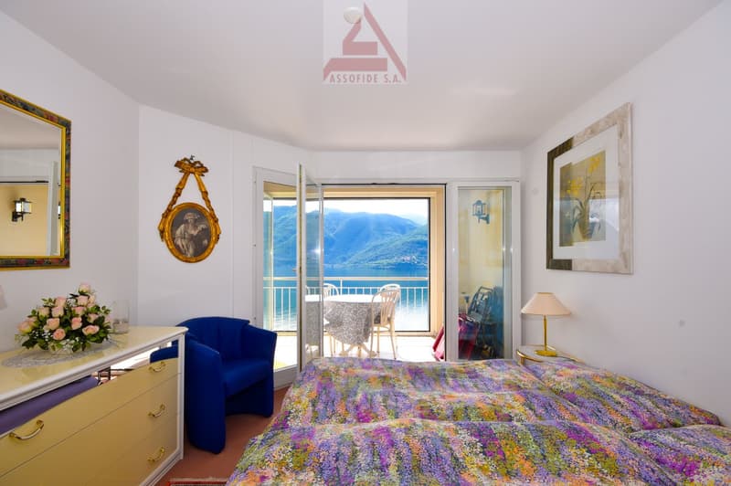 blue armchair, floral bedspread, white dresser, balcony with outdoor table and chairs, framed picture on wall, mirror