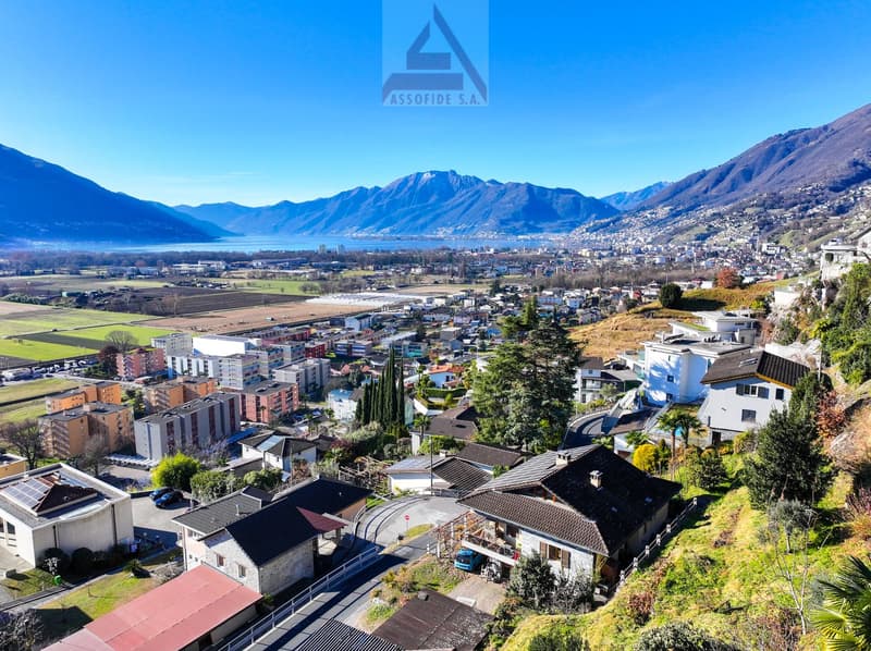 Aerial view of houses on hillside with lake, mountains, and a city in the background.