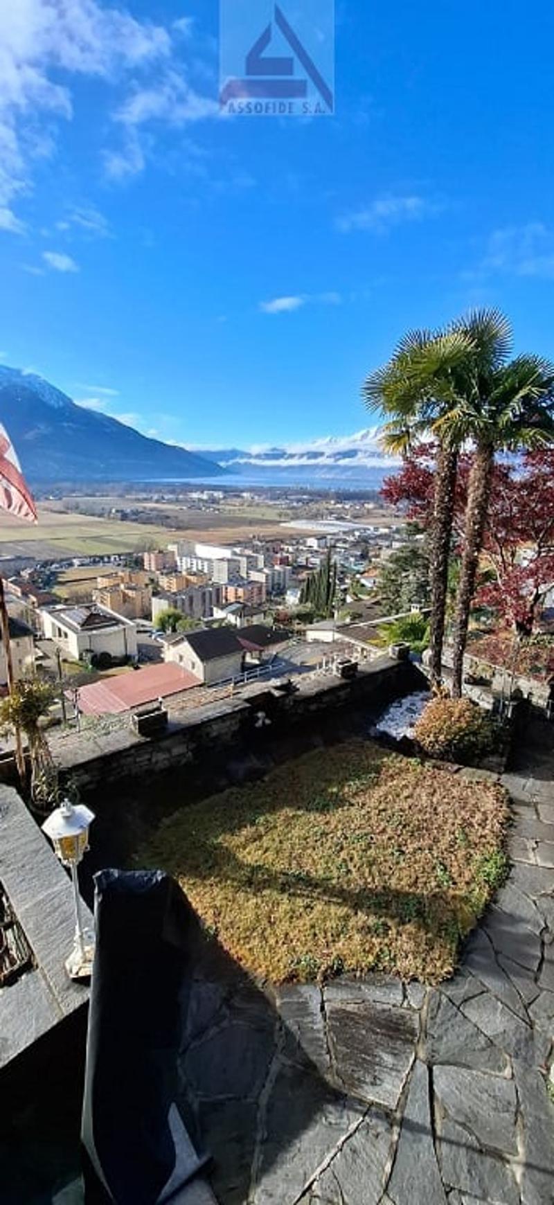 Aerial view of a garden with grassy lawn, palm tree, pathway, lamp, fence with an expansive view of a town and mountains