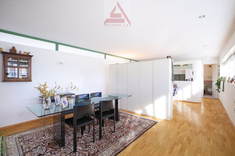 Glass table with four black chairs, wood floor, wall decorations, rug, cabinet with glass doors, white kitchen partition